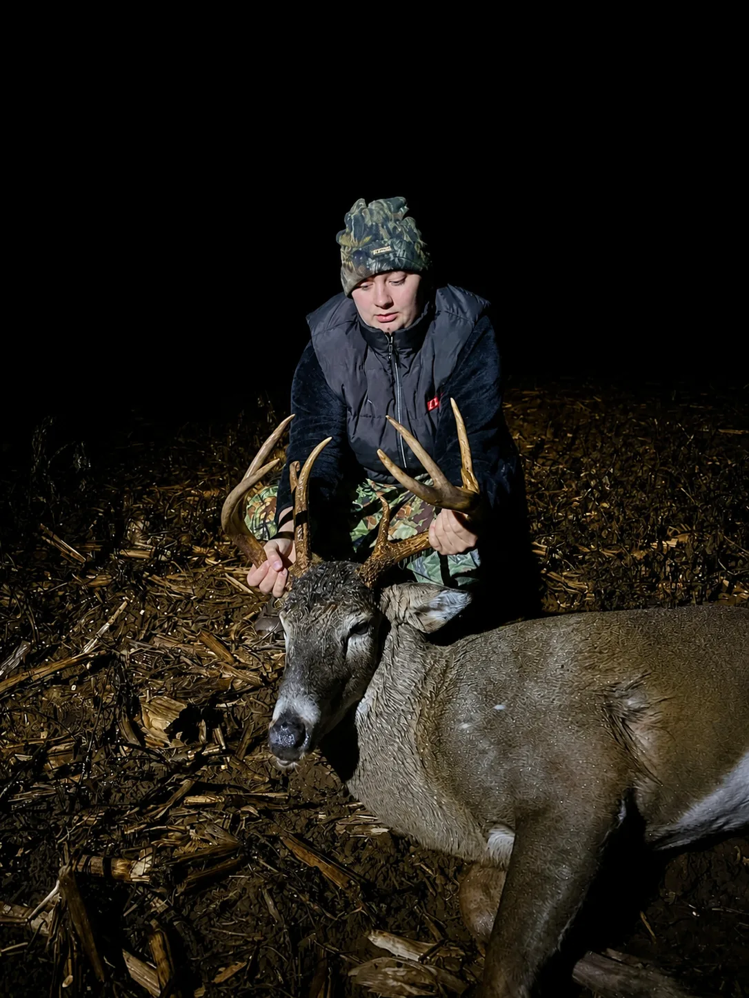 Hunter posing with a whitetail buck in a cornfield at night