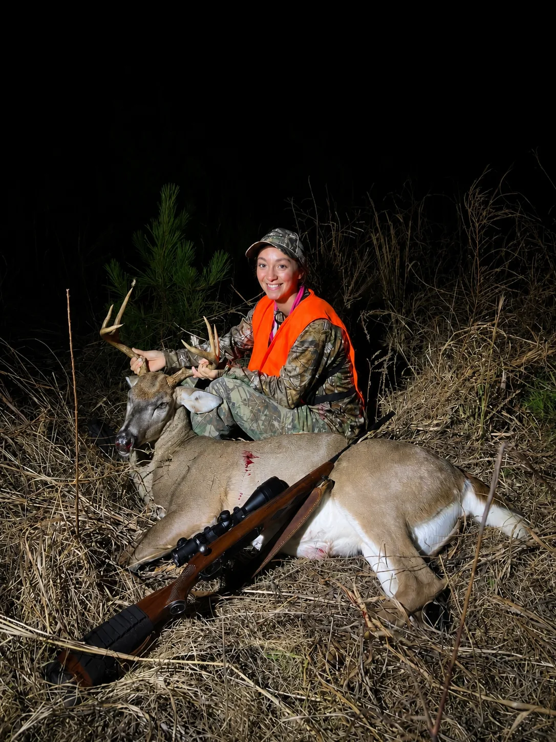 Hunter in orange safety vest with a whitetail deer at night