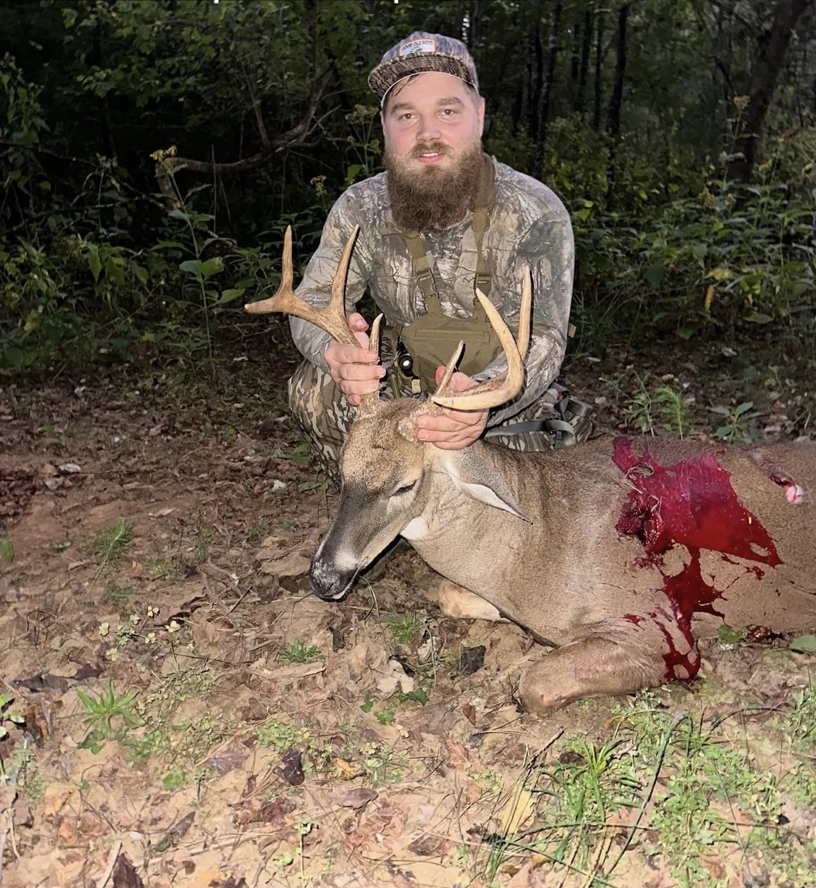 Hunter kneeling with a whitetail buck in the woods